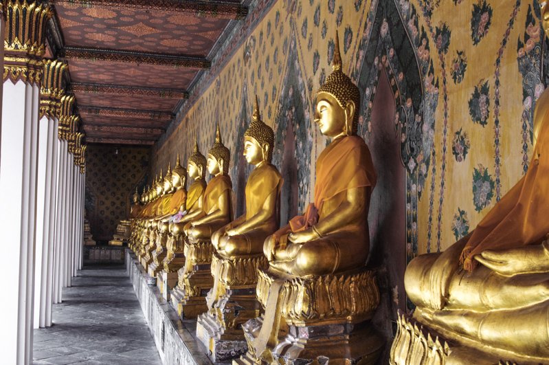 Gold buddhas lined up against wall at Temple of Reclining Buddha in Thailand