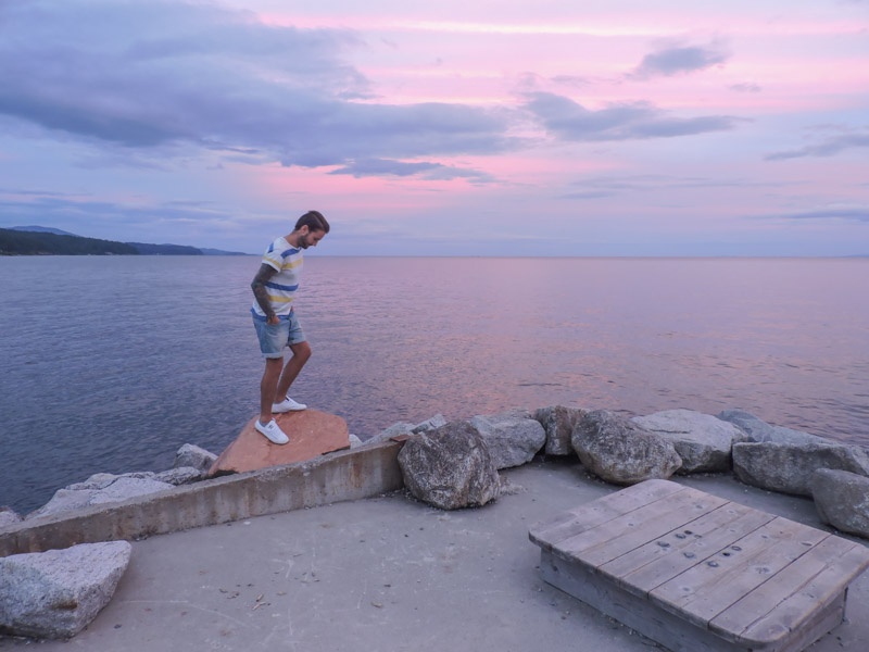 Man standing on large stone, ocean in background with pink sunset at Robert Creek Beach Pier_