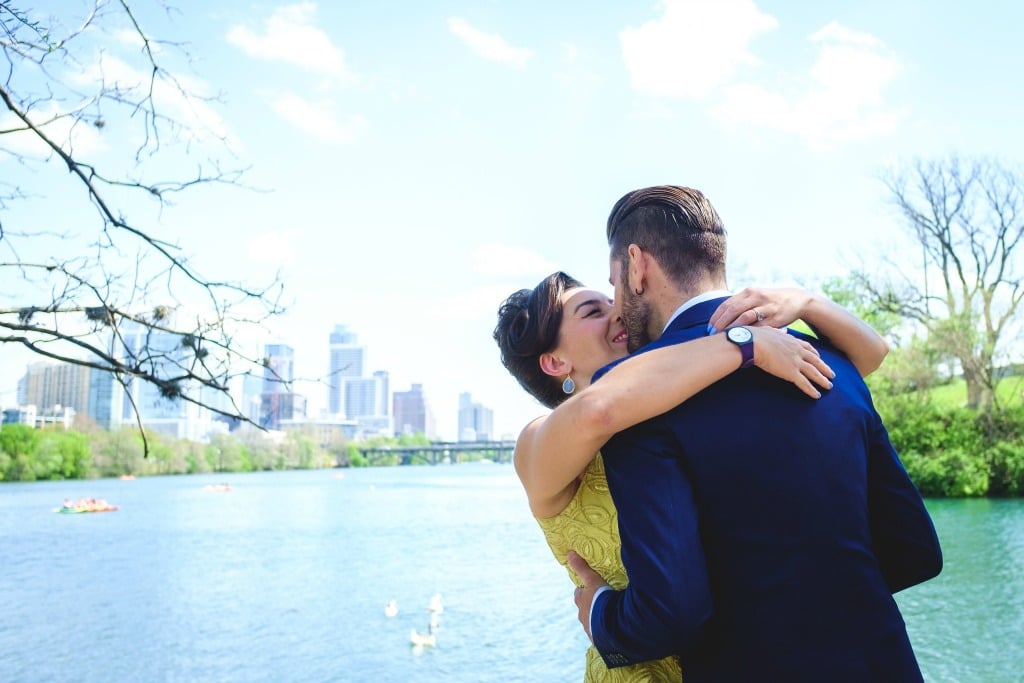 Bride in yellow dress, groom in navy suit kiss against Lady Bird Lake Austin backdrop