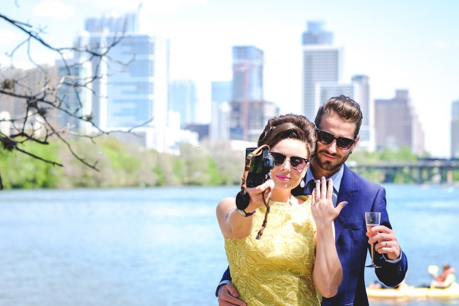 Bride in yellow dress, groom in navy suit, taking a selfie against Lady Bird Lake Austin backdrop