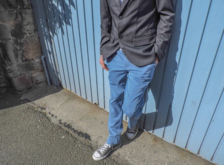 Man wearing light blue Bluffworks travel pants leaning against blue door