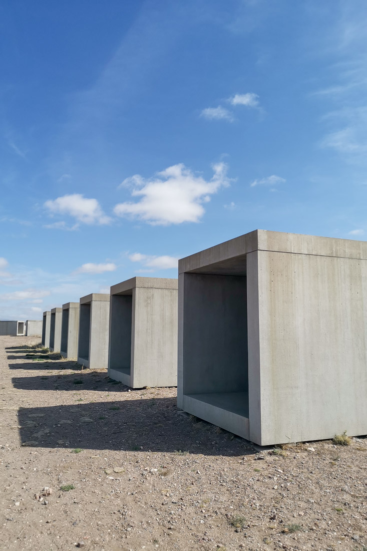15 Untitled Works in Concrete in Marfa Texas Grey concrete hollow boxes on sandy ground with blue skies and shadows