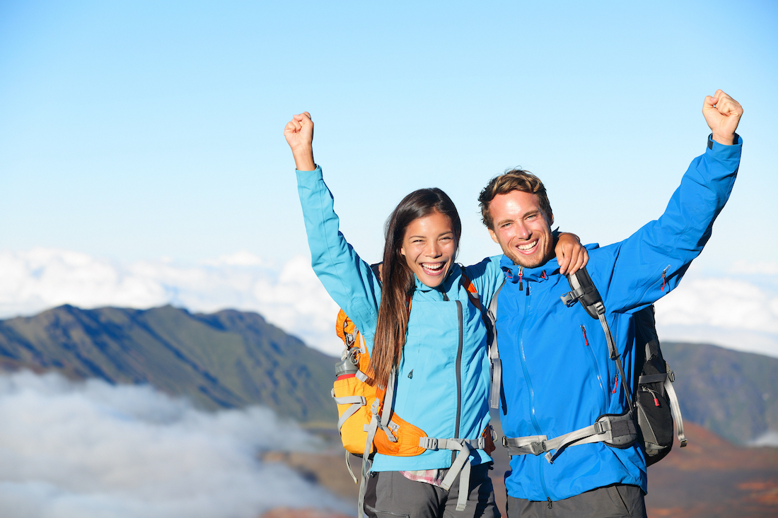 Hikers - people hiking cheering on summit top with view on volcano. Hiker couple looking at beautiful landscape of mountain volcanoes, Haleakala national park Hawaii, USA. People exited and happy.