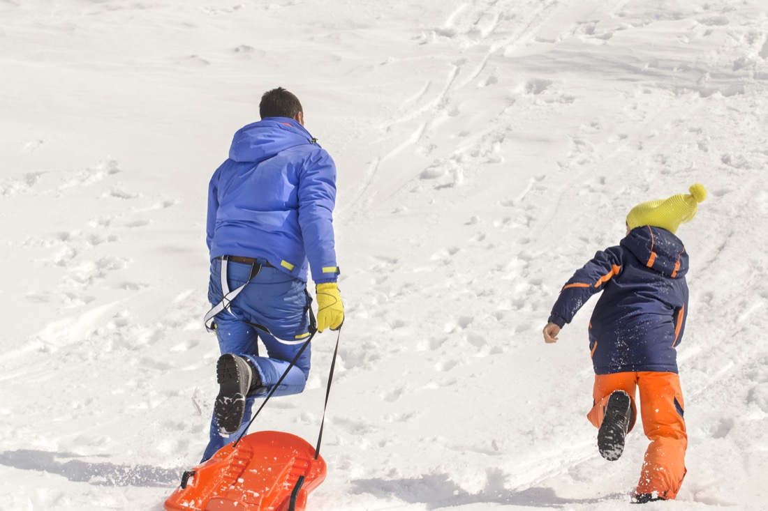 Father and son having fun sledding in the snow 