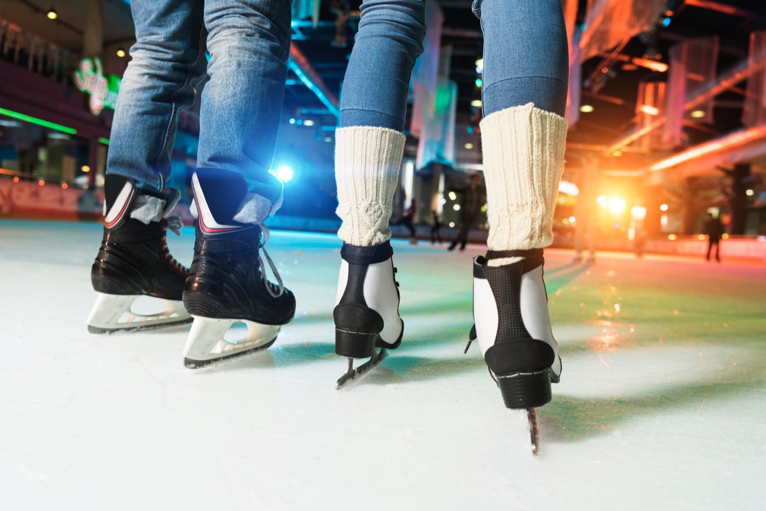 Low section of couple in skates ice skating on rink 