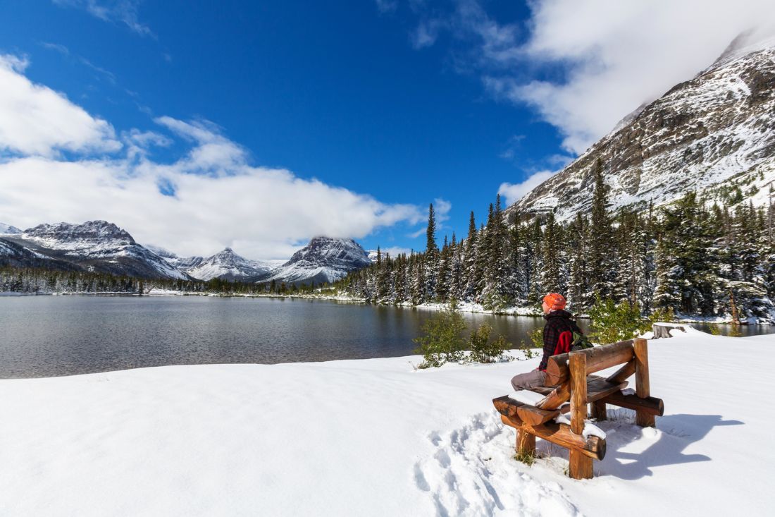 Scenic view of lake and snow with an sitting on a bench at Glacier National Park in winter