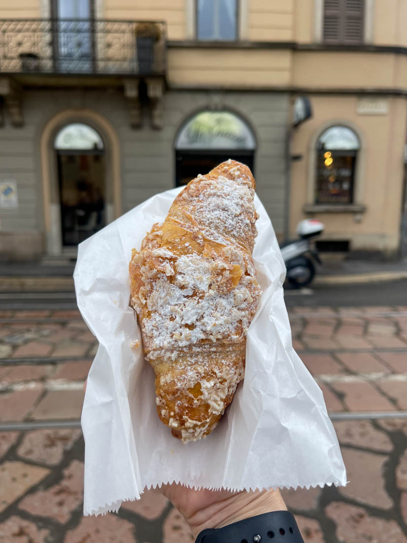 Hand holding croissant at Piazza Santa Maria delle Grazie in Milan